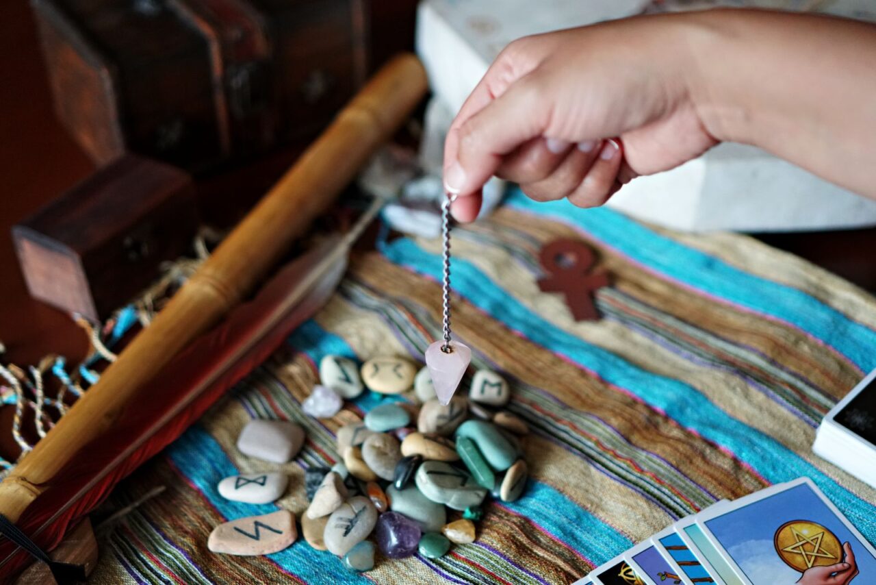 Mano utilizando un péndulo sobre minerales y símbolos